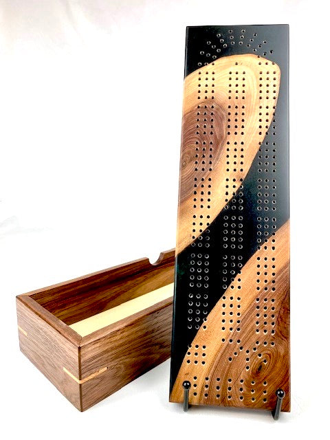 Handmade cribbage board made of black with green accents resin and walnut that doubles as a lid to a storage box made of walnut with maple accents.
