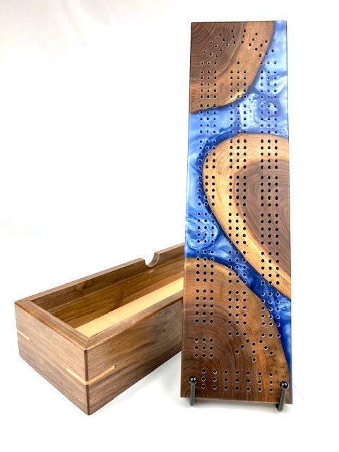 Handmade cribbage board made of iceberg blue resin and walnut that doubles as a lid to a storage box made of walnut with maple accents.