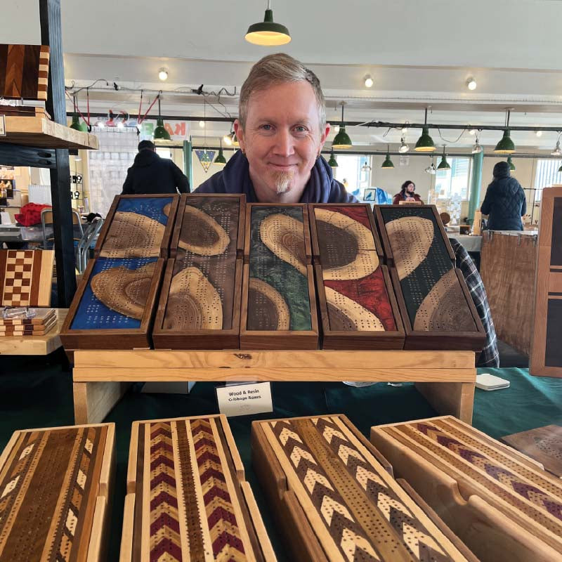 Man standing behind a display of wooden art pieces at Pike Place Market.